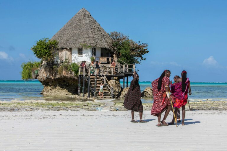Cultural scene with The Rock restaurant and locals in traditional attire on a Zanzibar beach.